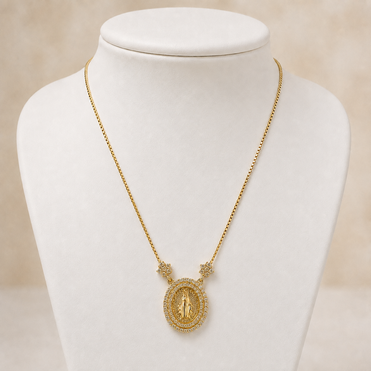 A gold necklace displayed on a white jewelry bust against a soft beige background. The necklace features a delicate gold chain with small gold star-like links, a central oval medallion with a raised figure, and a border of small clear stones.