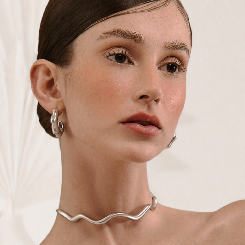 Close-up of a woman wearing silver hoop earrings and a silver necklace against a neutral background
