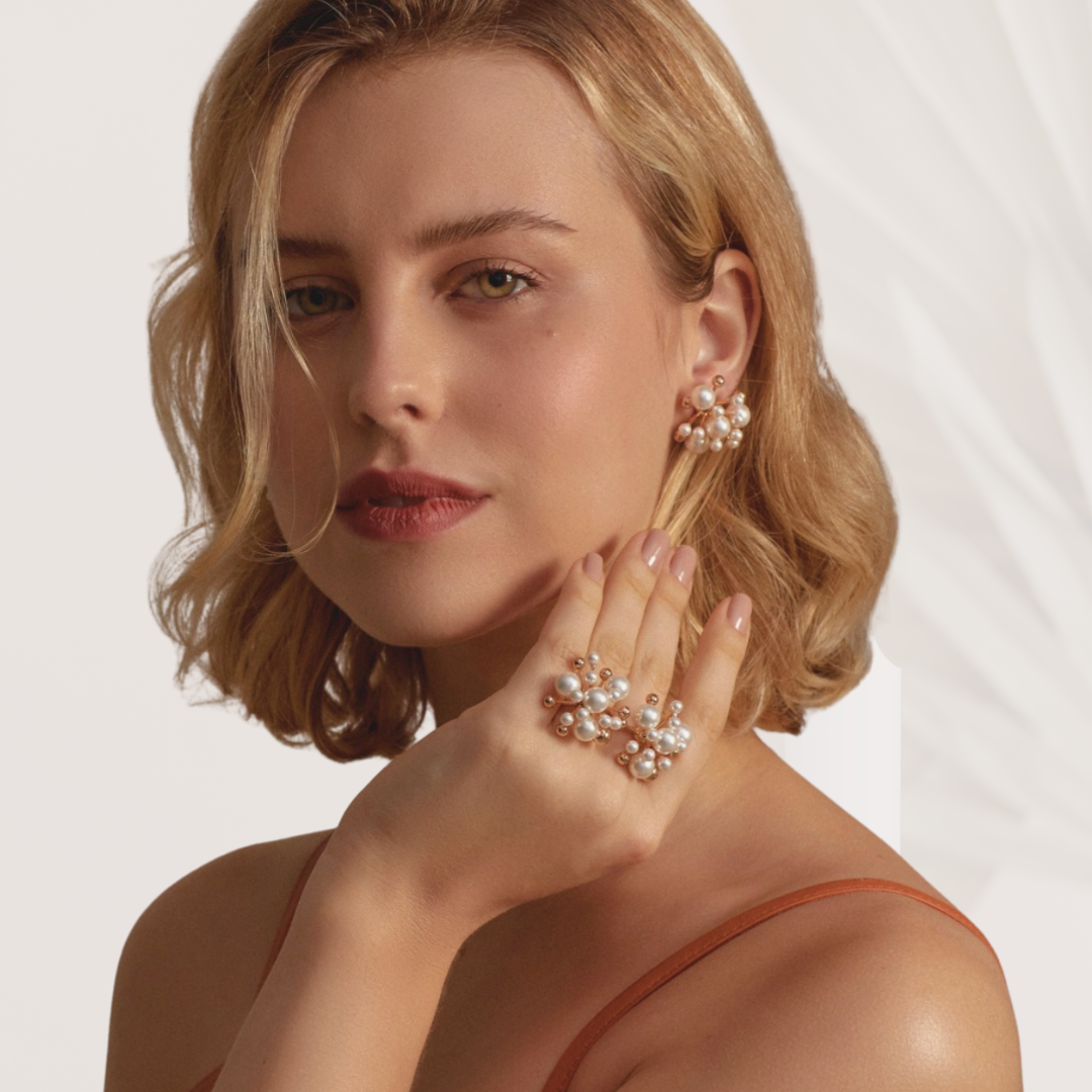 Woman wearing pearl earrings and ring against a plain background