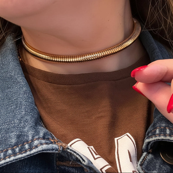 Close-up of a person wearing a gold necklace, brown shirt, and denim jacket.