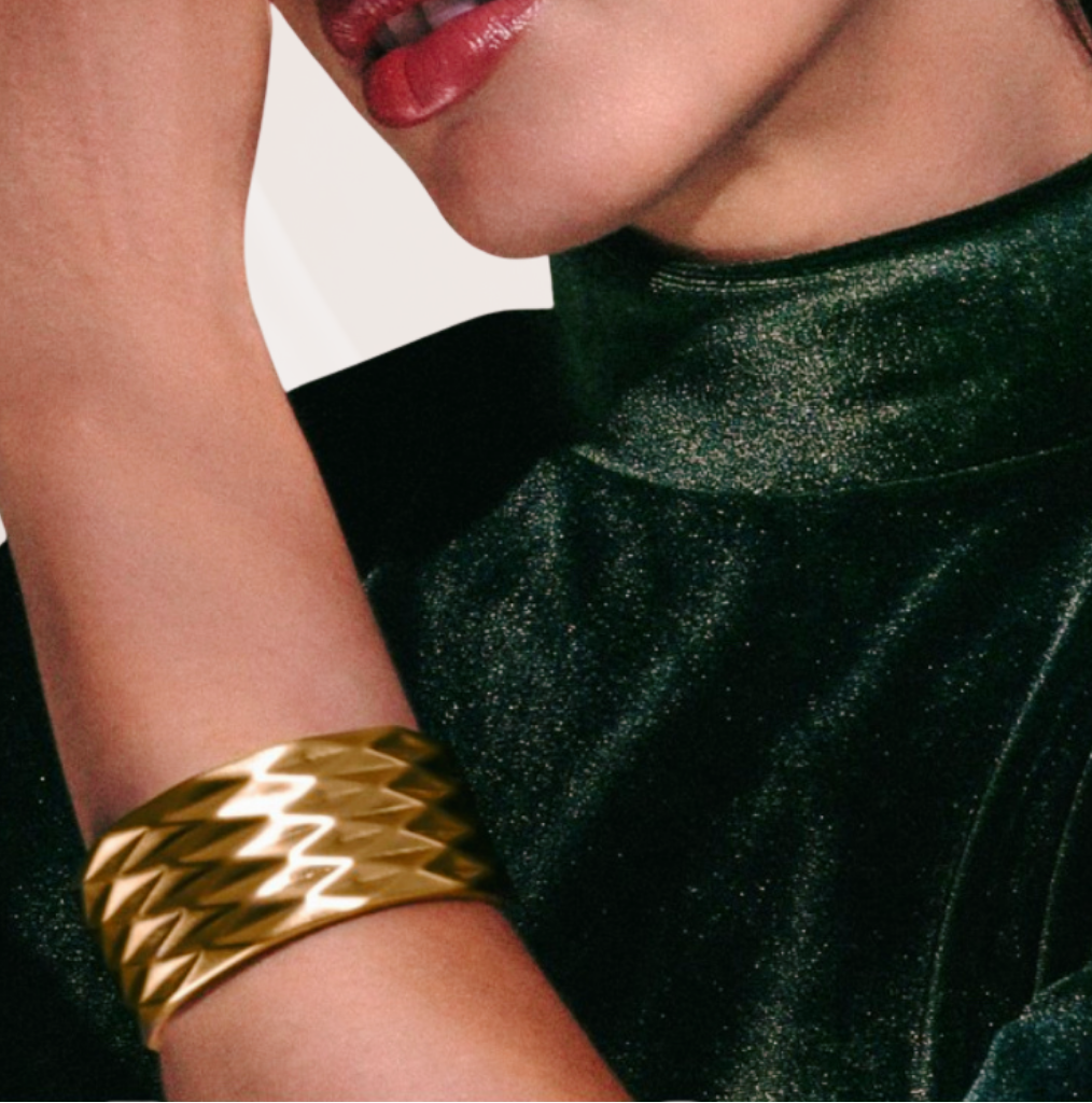 Close-up of a person wearing a gold bracelet on a plain background