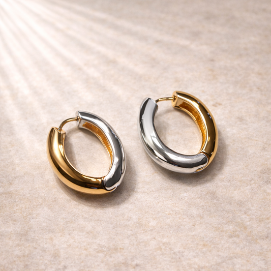 Pair of gold and silver hoop earrings on a beige surface