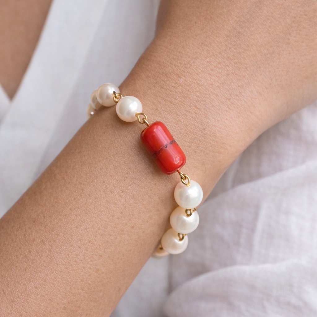 Bracelet with pearls and a red bead on a wrist against a white background