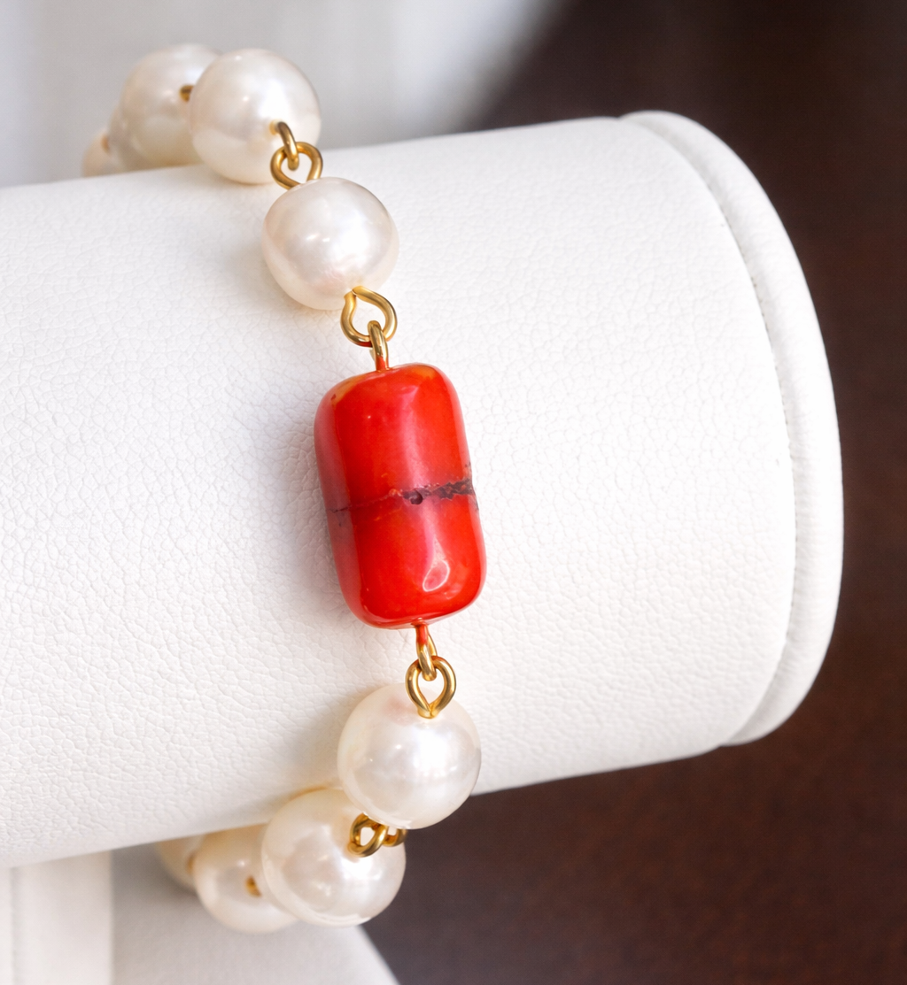 Pearl and red bead bracelet on a white cylindrical stand with a blurred background