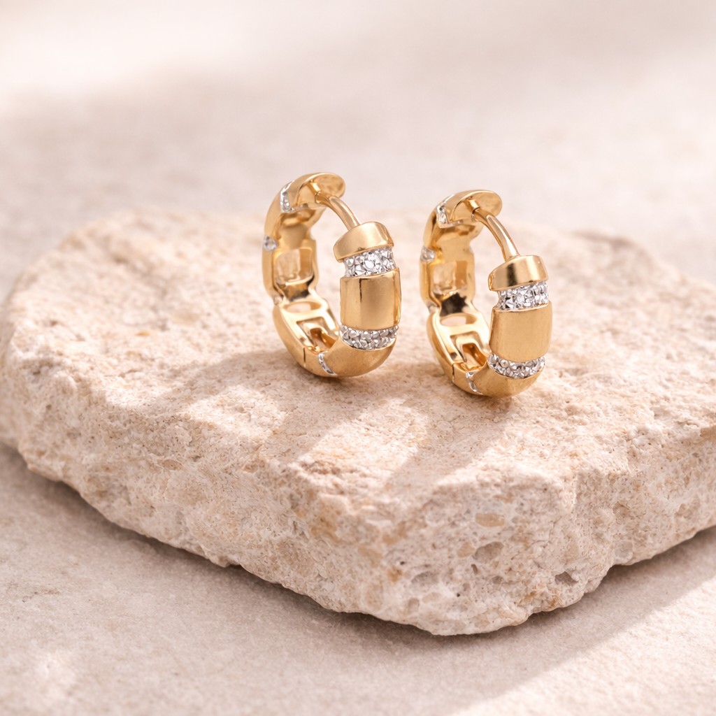 Gold hoop earrings with small diamonds on a light stone surface