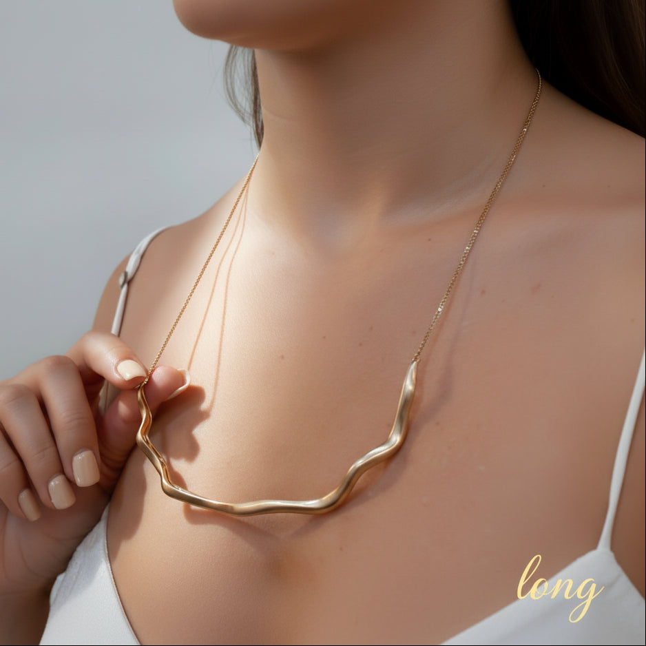 Gold necklace being held up to a person wearing a white lace top.