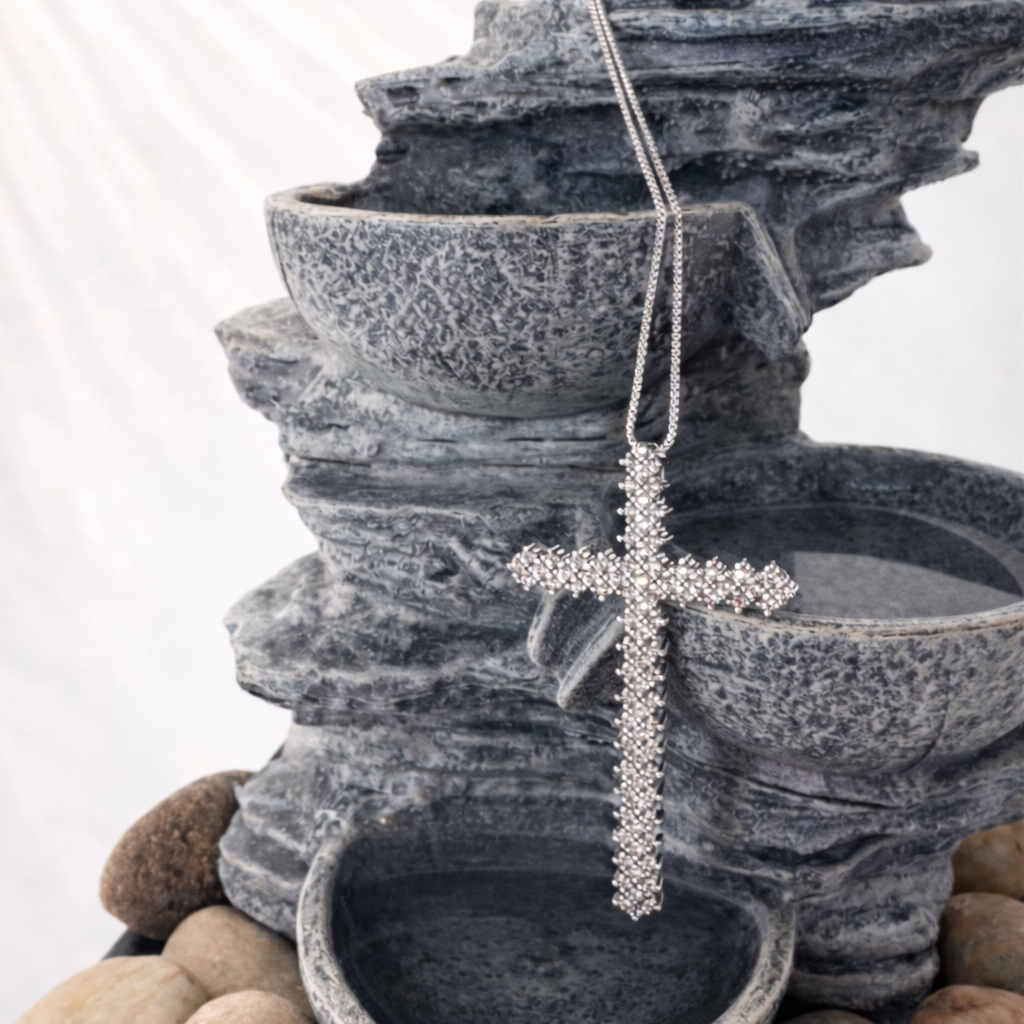 Decorative cross necklace on a stone fountain with pebbles.