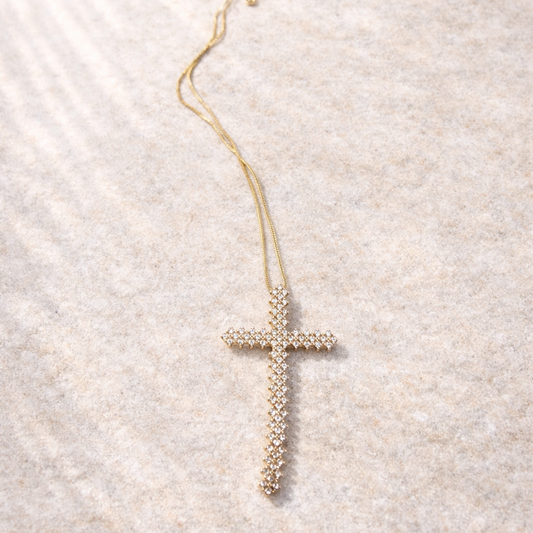 Gold cross necklace on a textured beige surface