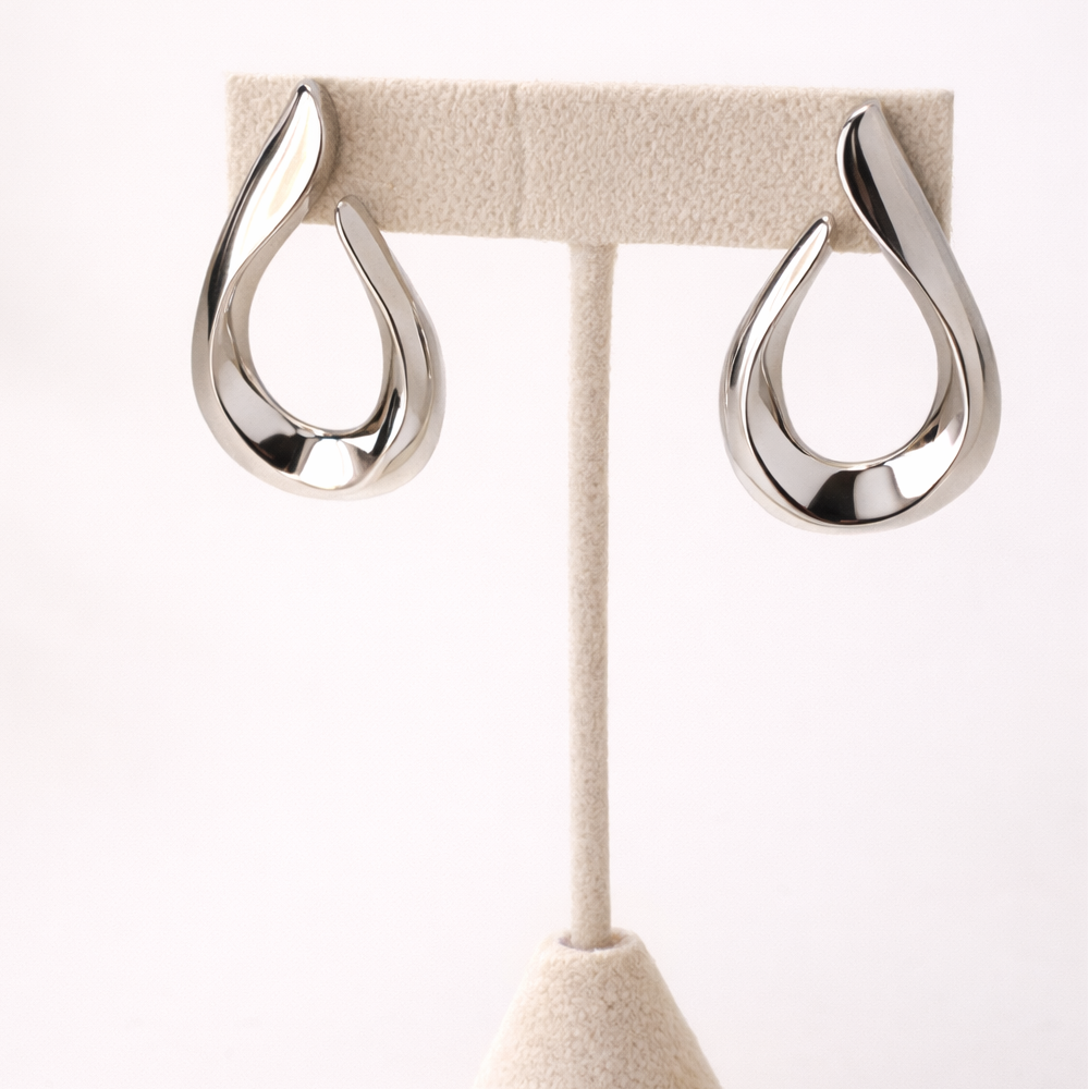 Silver earrings on a beige stand against a white background