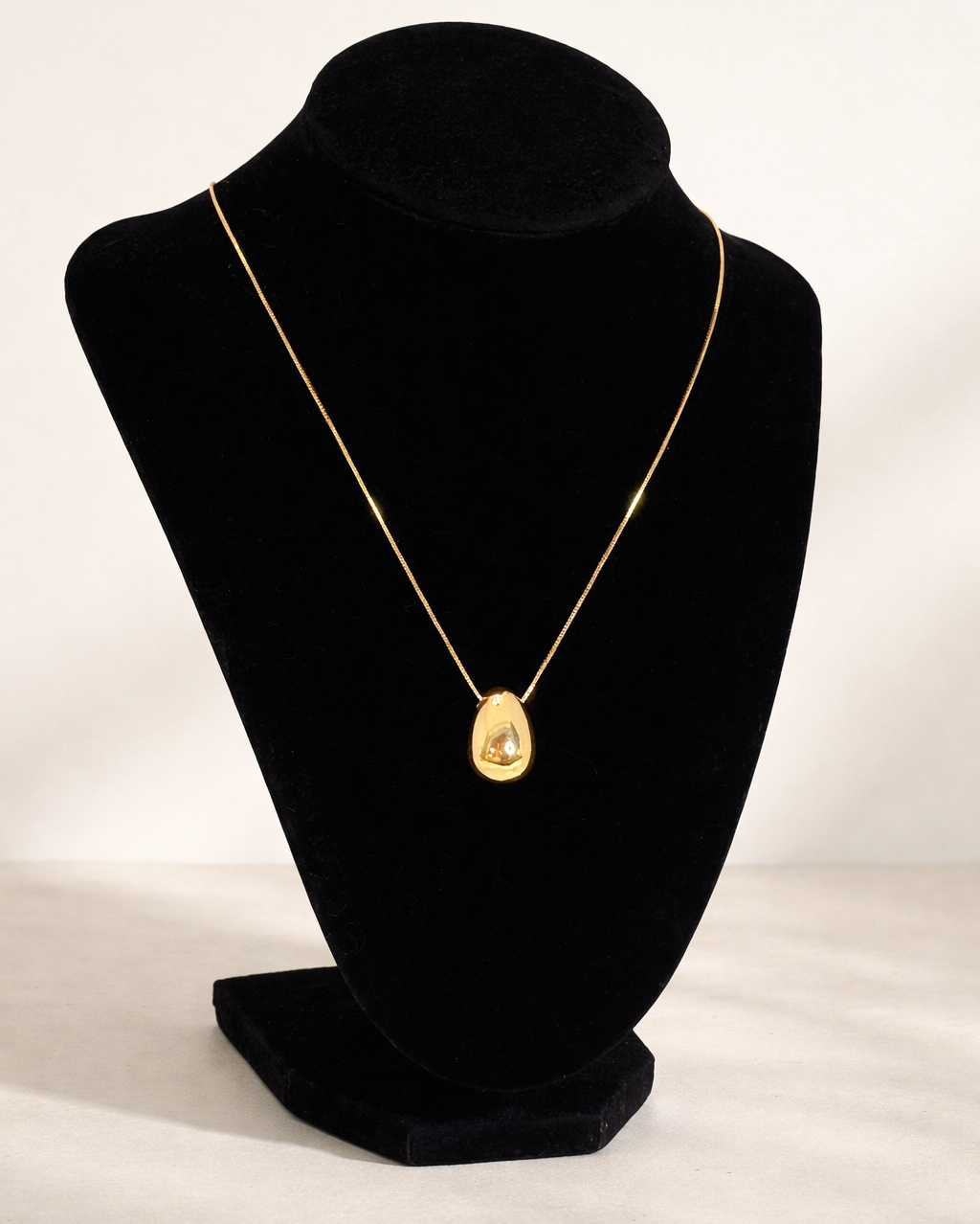 Gold necklace on a black velvet bust against a white background