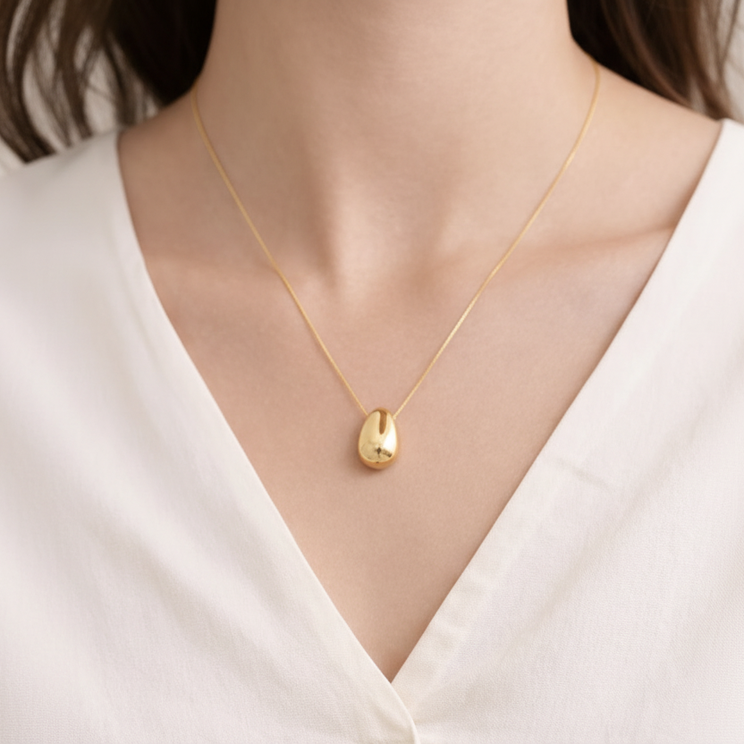 Gold necklace with a pendant on a person wearing a white top