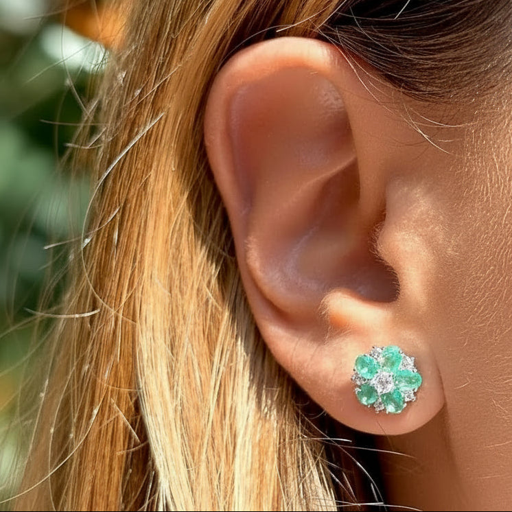 Close-up of an ear wearing a floral stud earring with green gemstones.