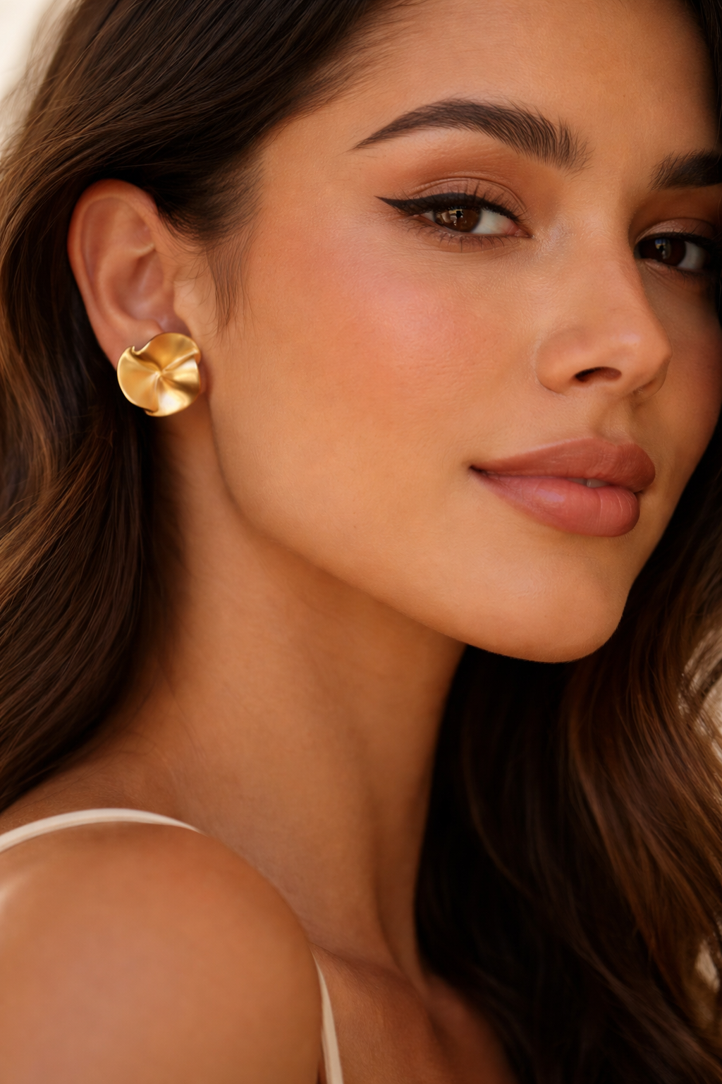 Close-up of a woman wearing gold earrings with a neutral background