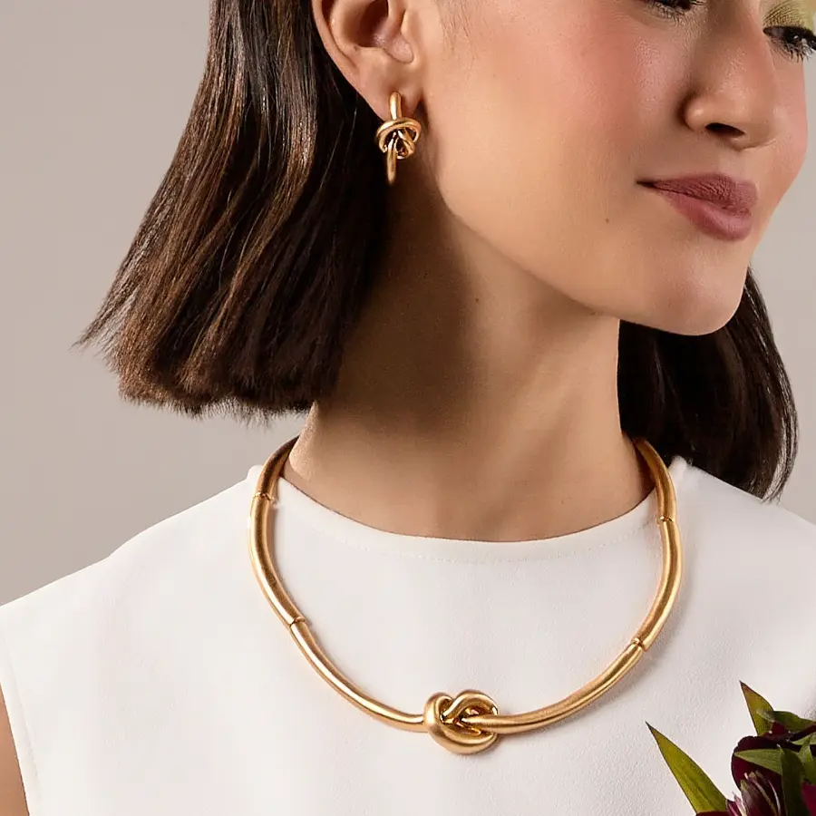 Woman wearing a gold necklace and earrings against a neutral background