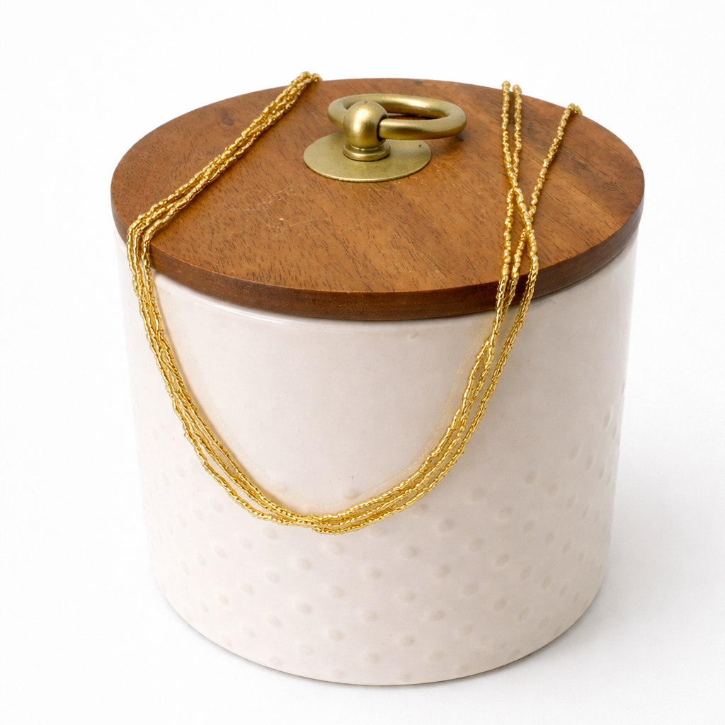 Cylindrical ceramic container with wooden lid and gold chain on a white background