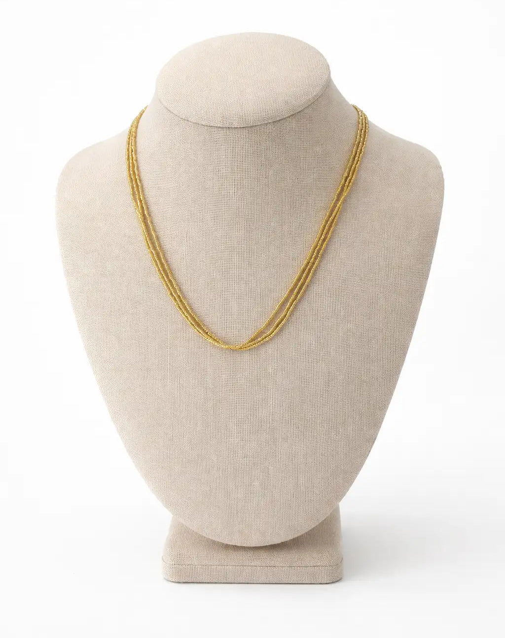 Gold swarovski  necklace on a beige mannequin bust against a white background