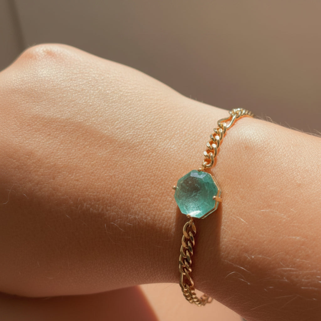 Gold bracelet with a green crystal on a wrist, inside a car.