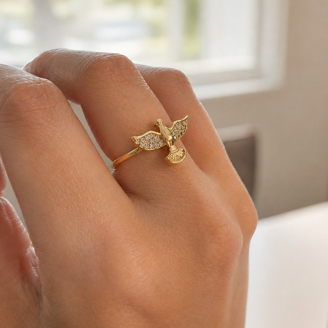 Hand wearing a gold ring with a butterfly design against a blurred indoor background