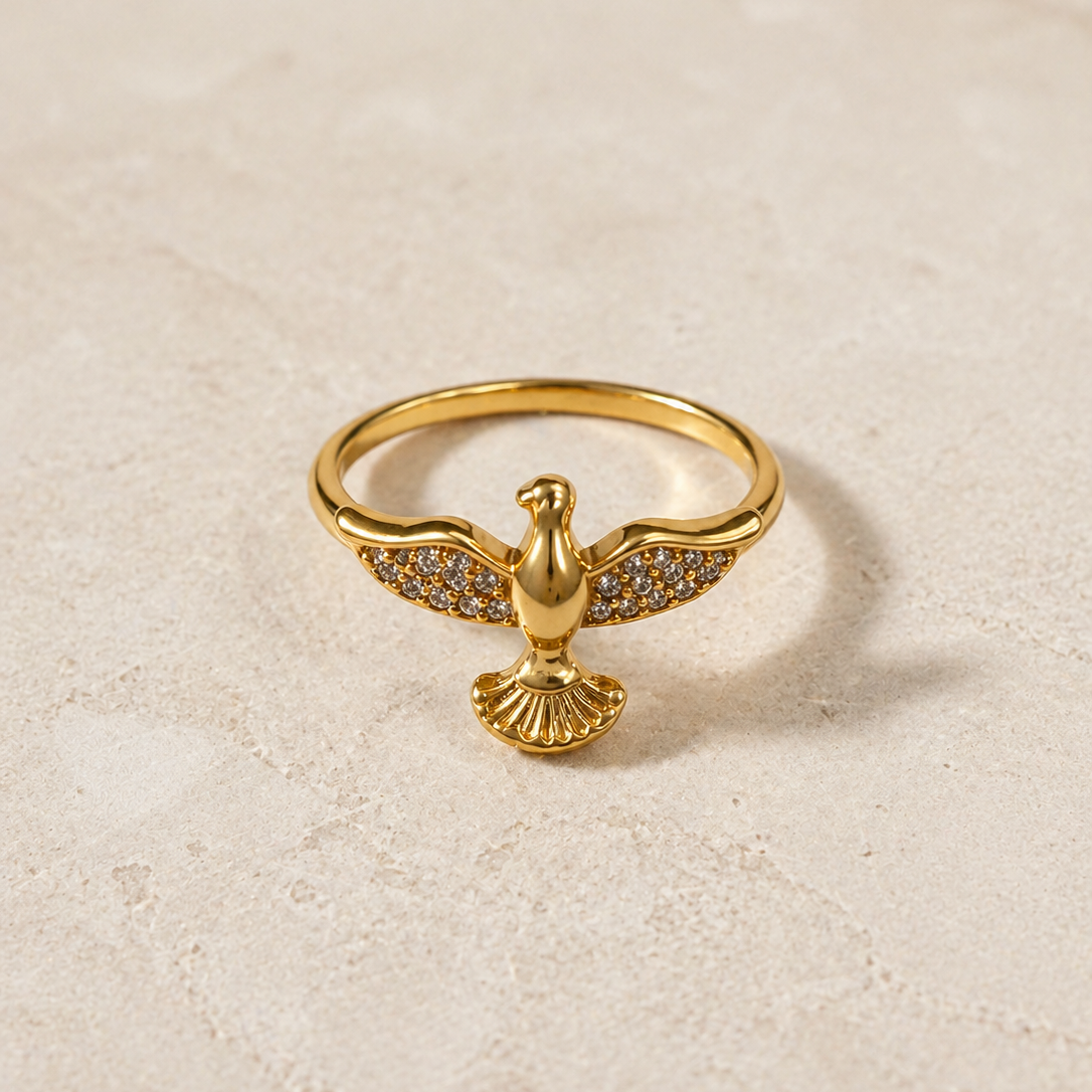 Gold eagle-shaped ring with embedded stones on a beige background