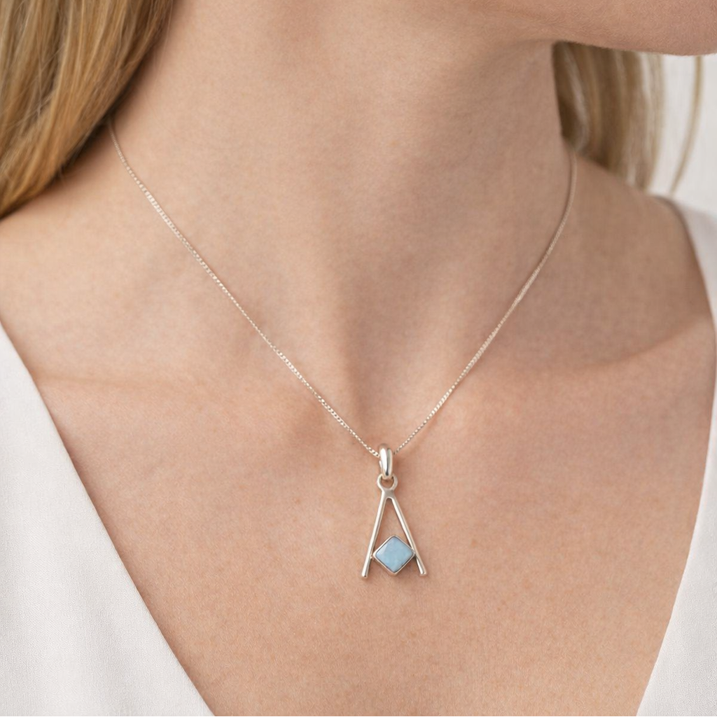Close-up of a person wearing a necklace with a pendant and matching earrings.