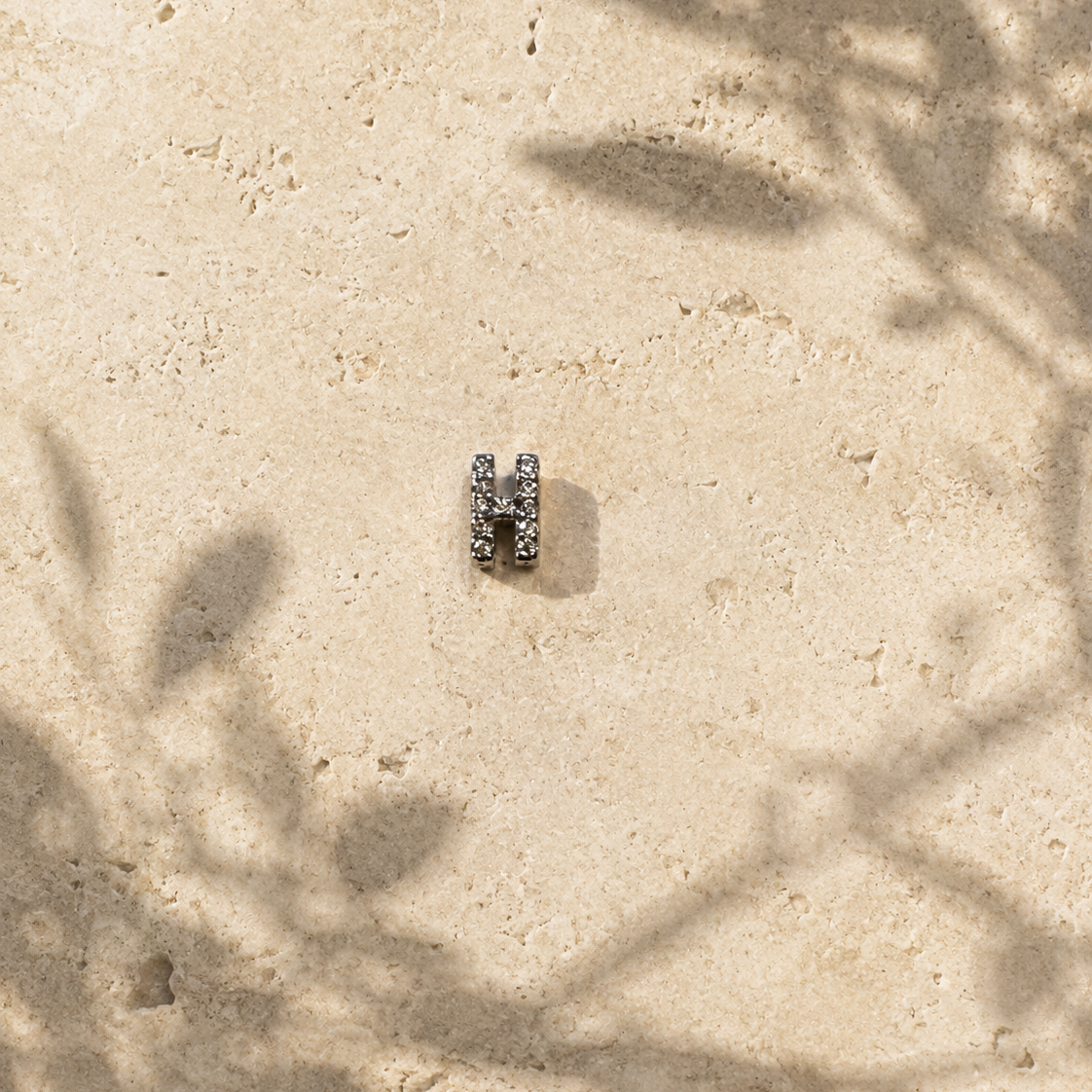 Small silver ring on a sandy surface with plant shadows
