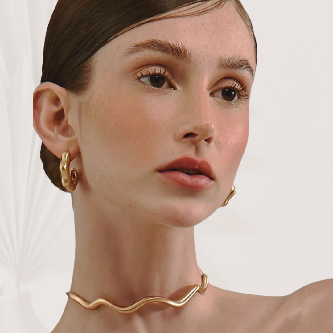 Close-up of a woman wearing gold hoop earrings and a gold necklace against a white background