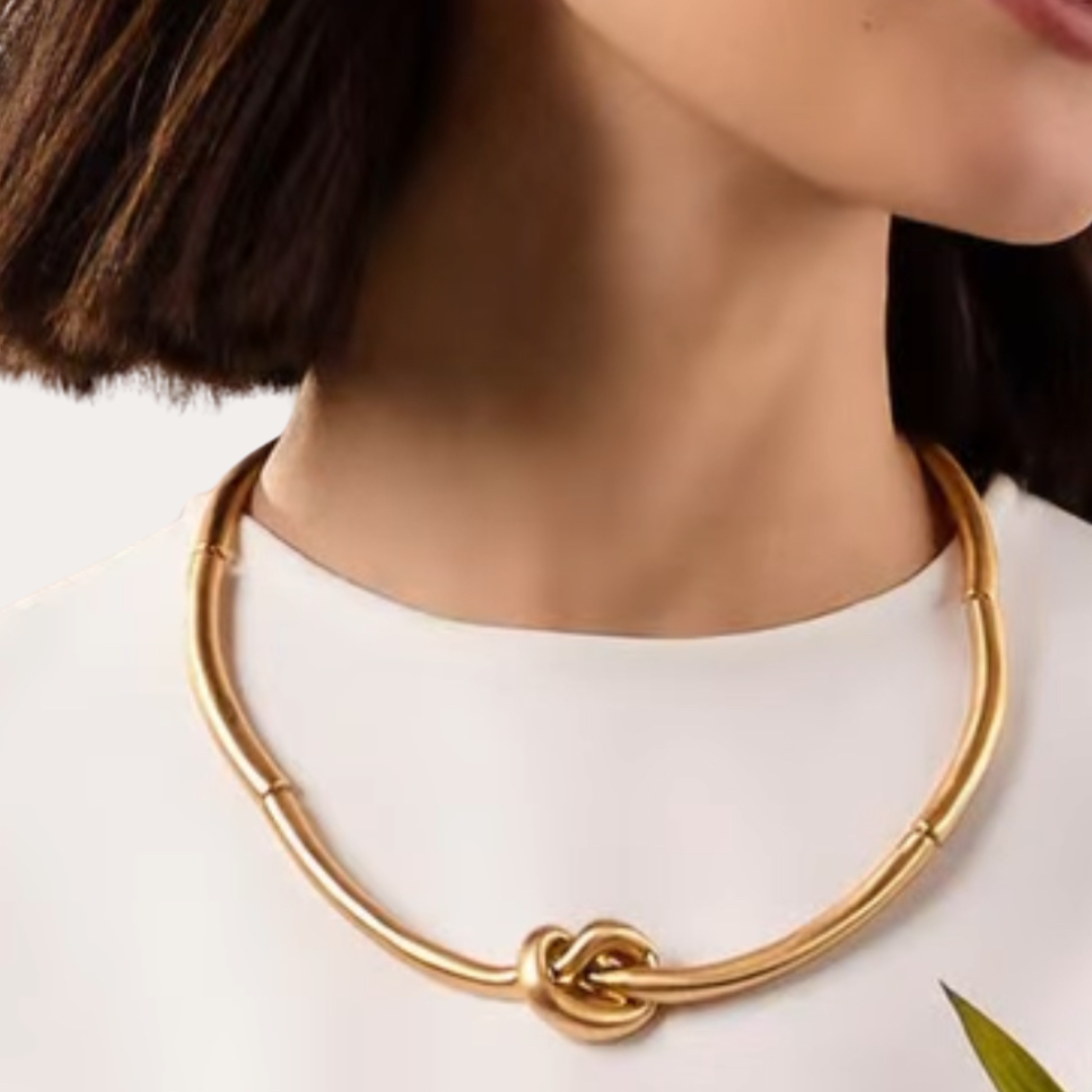 Gold necklace with a knot design worn by a person on a white background