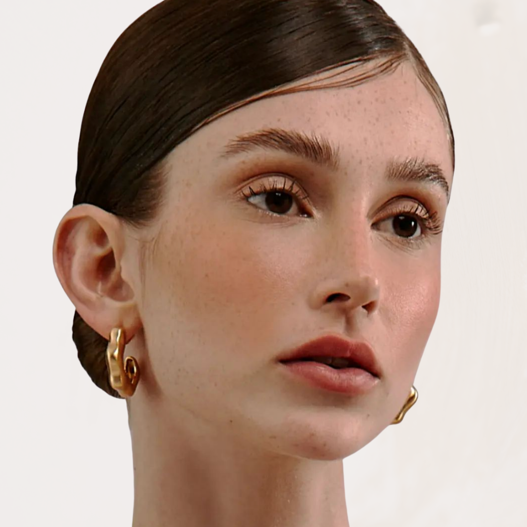Close-up of a person wearing gold hoop earrings on a plain background