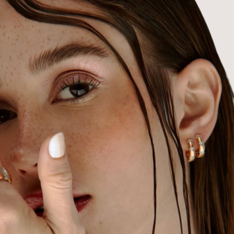 Close-up of a woman wearing gold earrings and rings on a neutral background