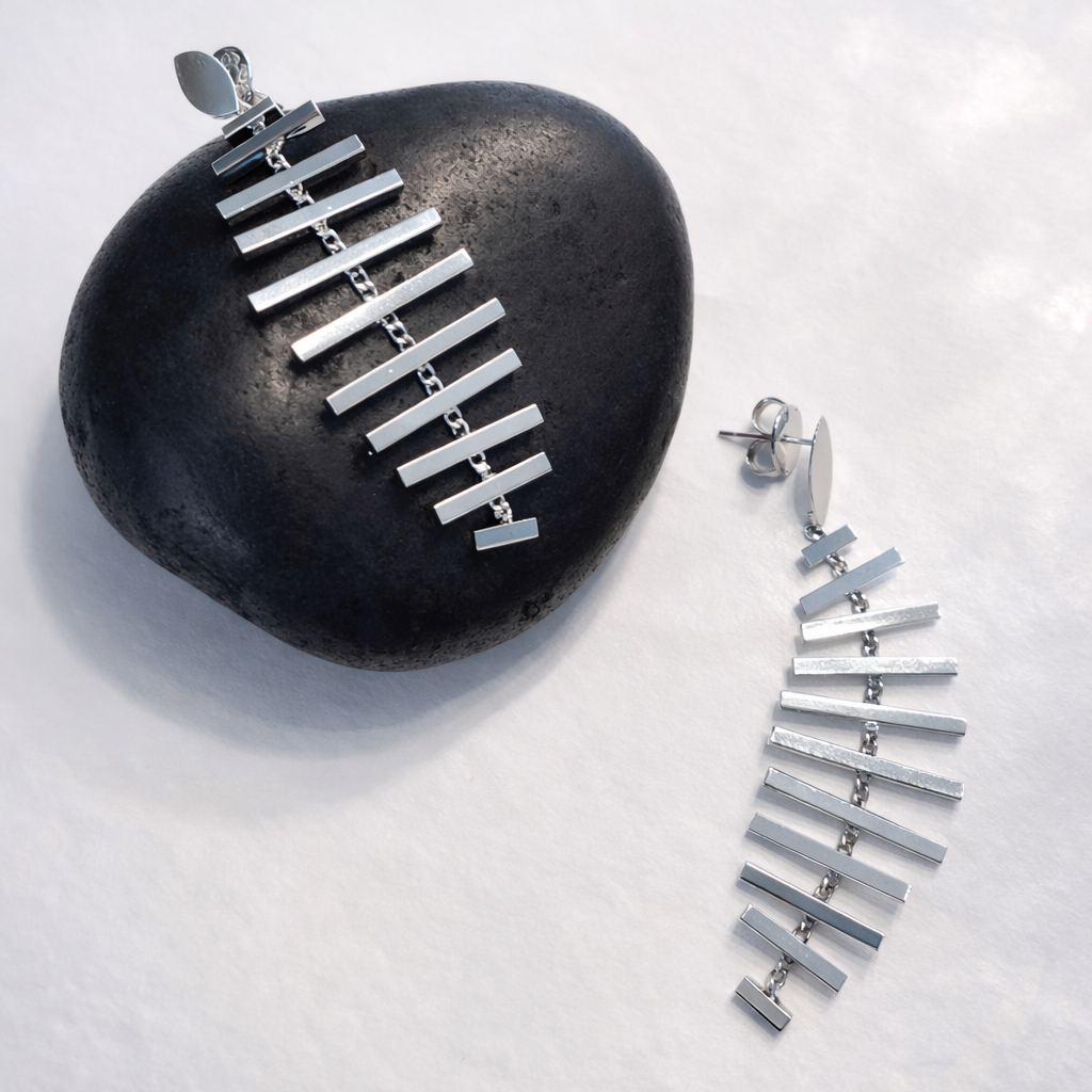 Silver mobile earrings on a dark stone with a light gray background