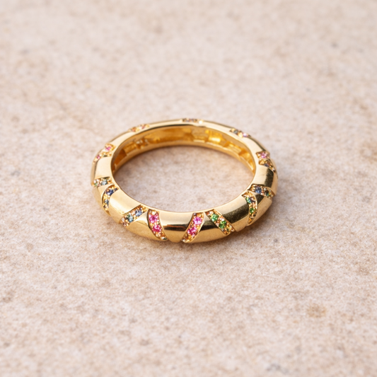 Gold ring with colorful gemstones on a beige surface
