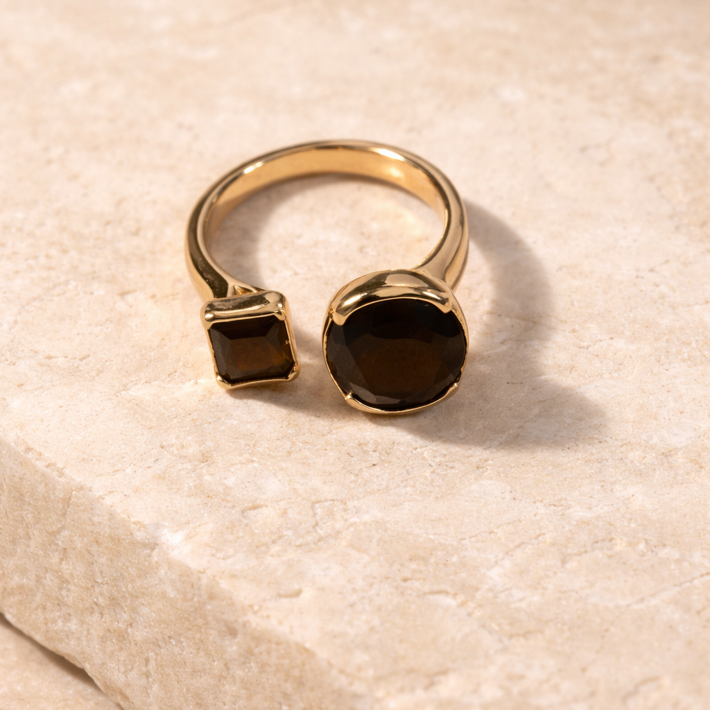 Gold ring with two dark gemstones on a textured beige surface