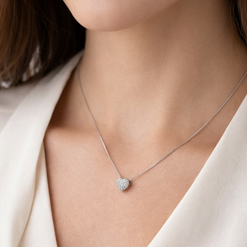 Necklace with a heart-shaped pendant worn by a person in a white outfit.