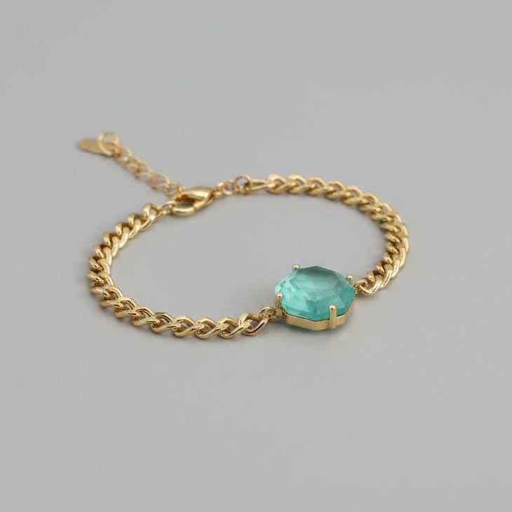 Bracelet with a green gemstone on a wrist against a neutral background