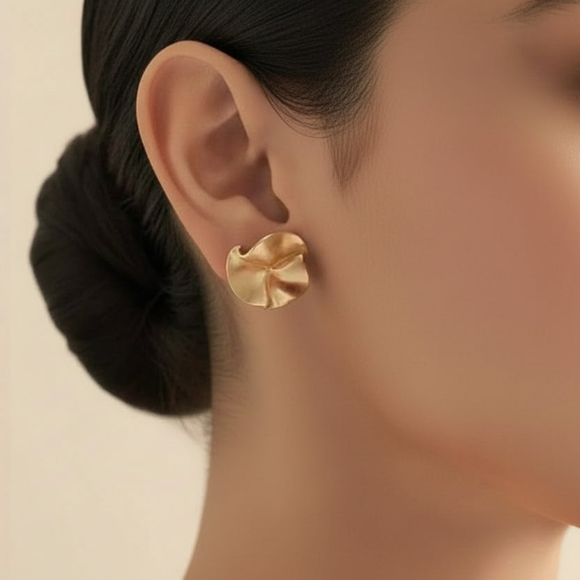 Gold earring worn on an ear with a model ear and white background
