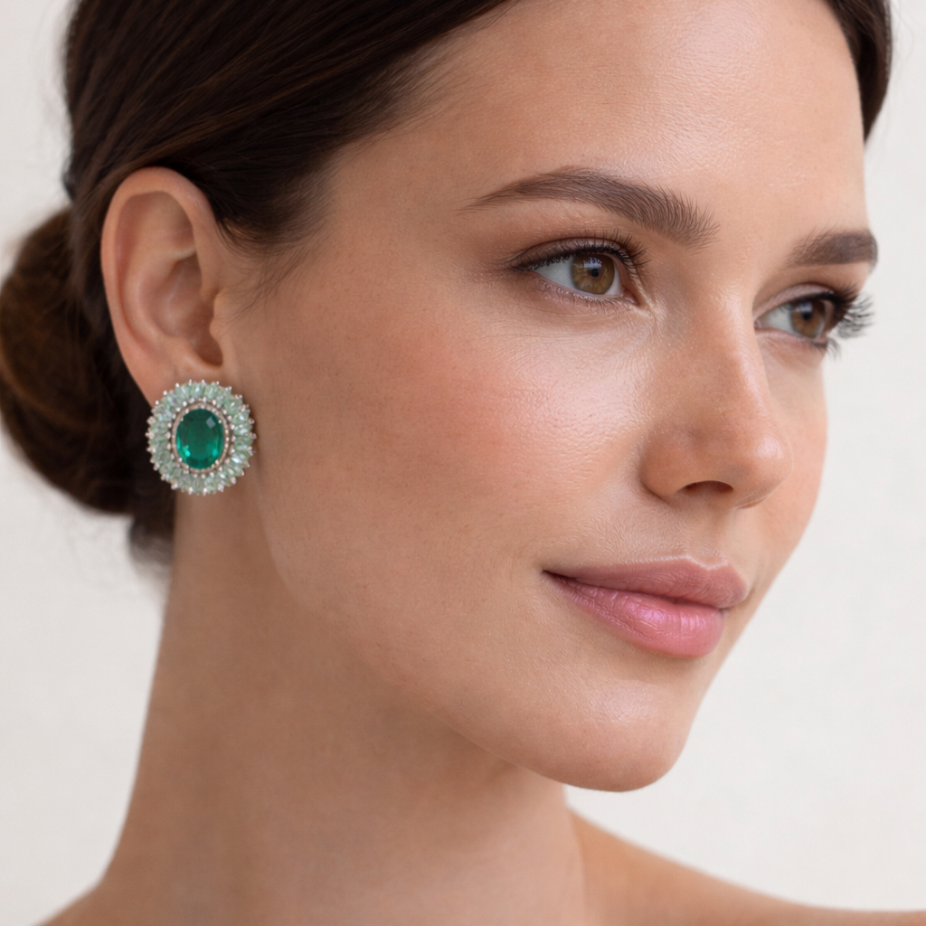 Woman wearing a pair of earrings with a green gemstone on a plain background