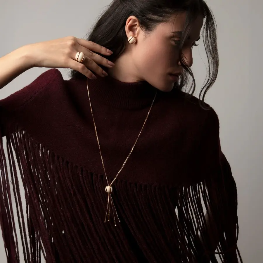 Woman wearing a dark brown fringe sweater with a plain background wearing a beautiful set of jewelry