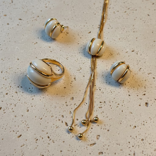 Jewelry set with gold and white earrings and ring on a textured surface