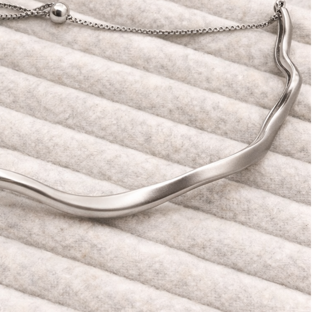 Silver necklace on a textured white surface with other jewelry items in the background