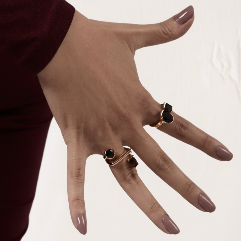 Hand wearing two rings with black stones on a plain background