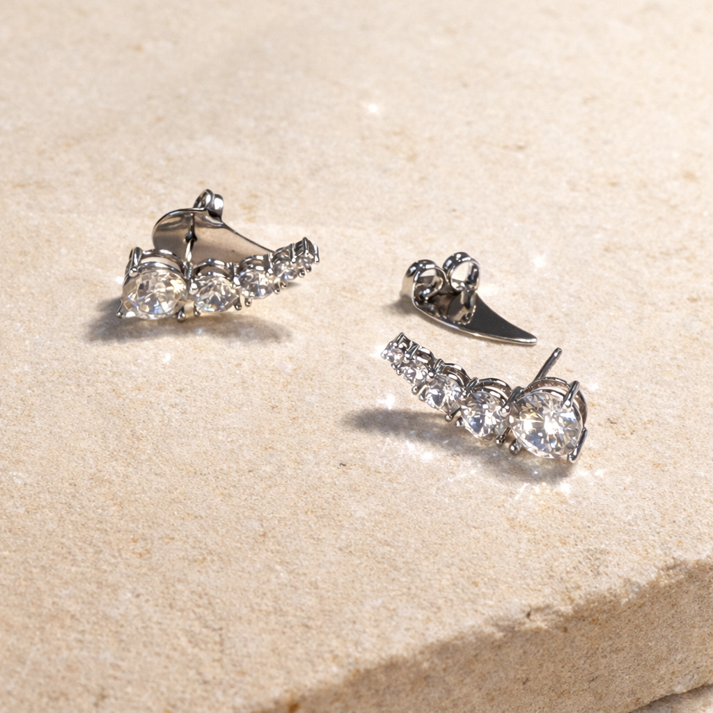 Pair of silver earrings with clear gemstones on a beige stone surface