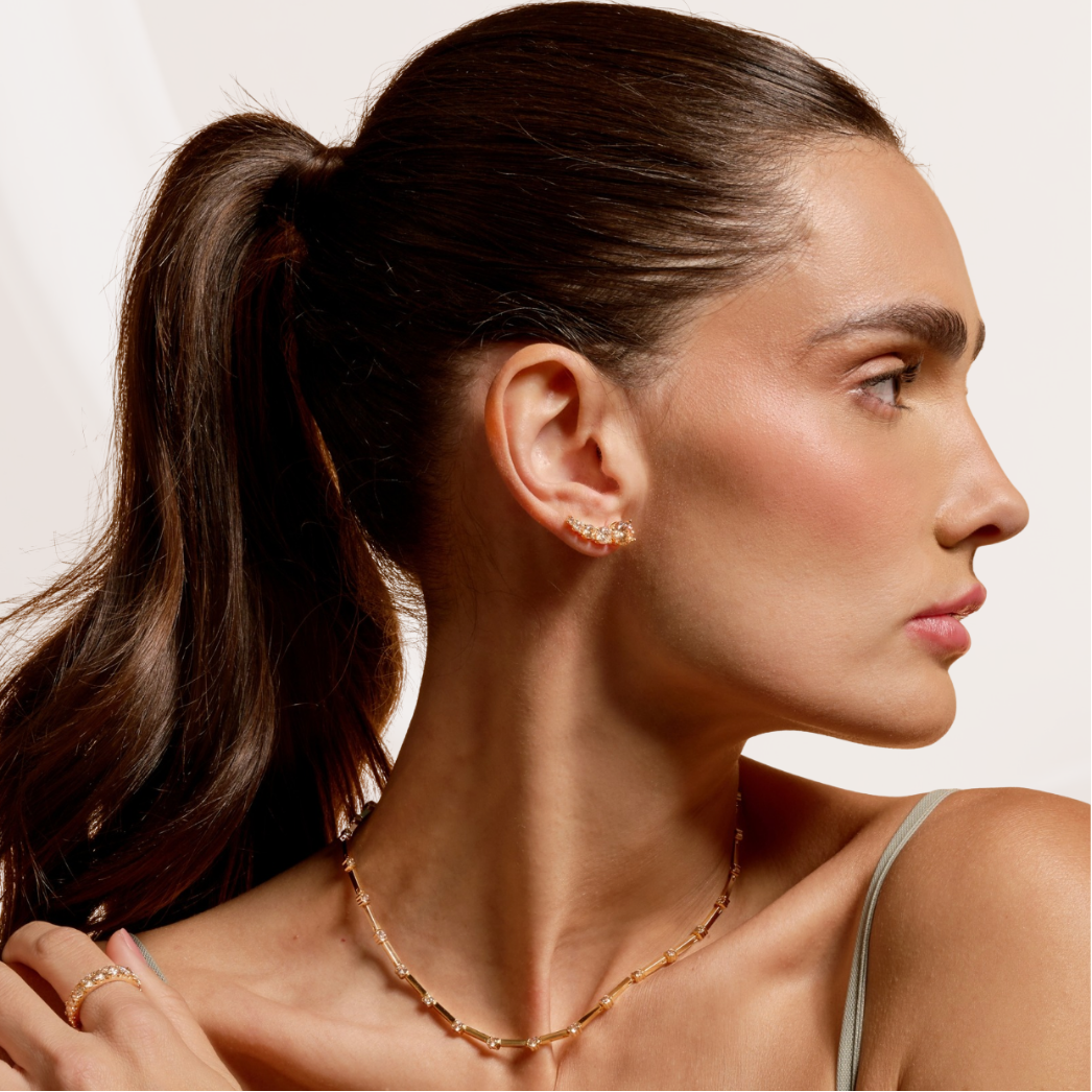 Woman wearing a gold necklace and earrings with a neutral background
