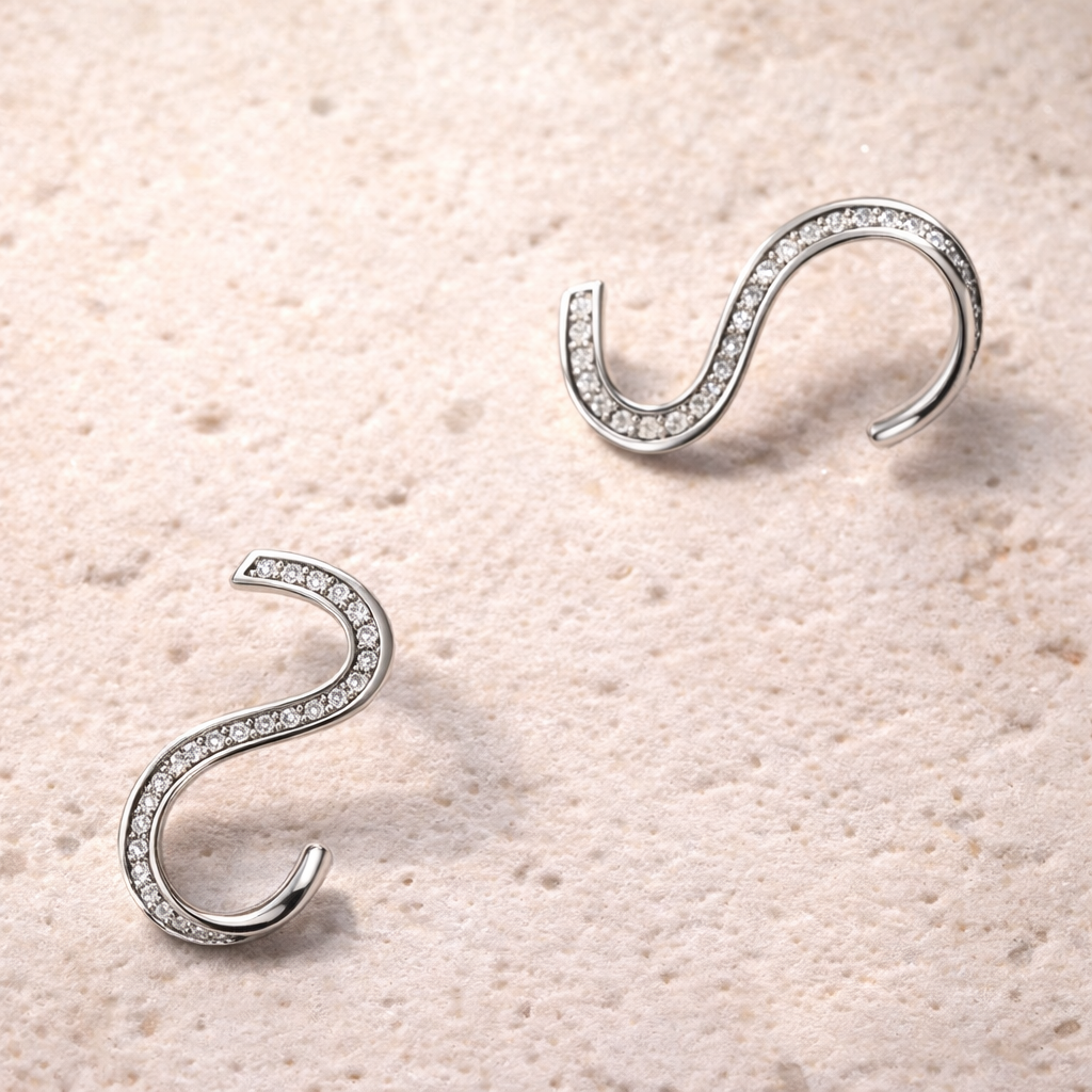 Silver curved earrings with zirconias on a beige textured background