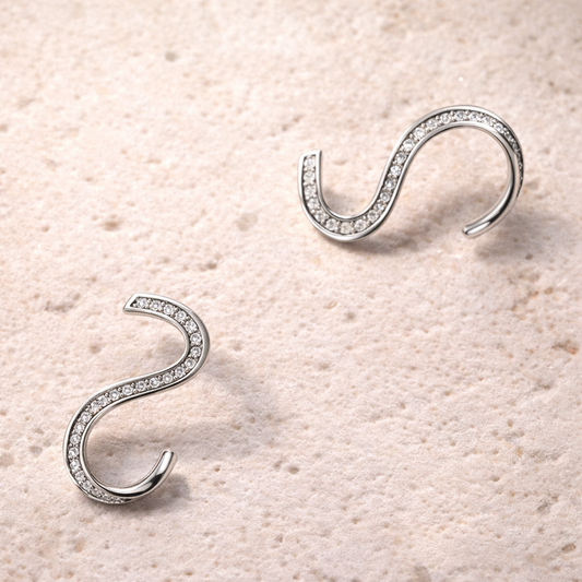 Silver curved earrings with zirconias on a beige textured background