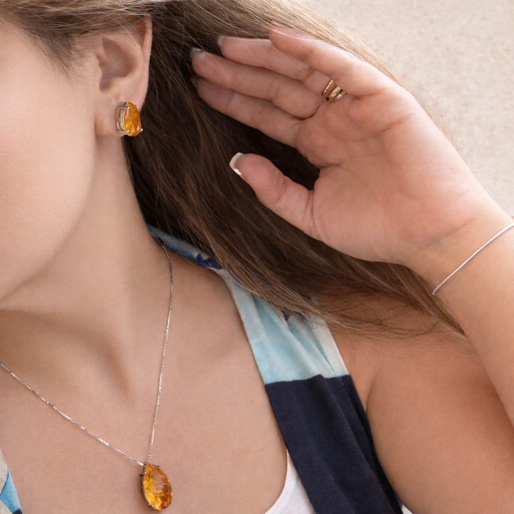Close-up of a person wearing amber-colored jewelry including earrings and a necklace.
