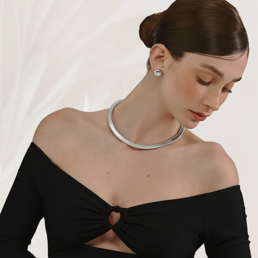 Woman wearing a beige off-shoulder top and gold necklace on a plain background