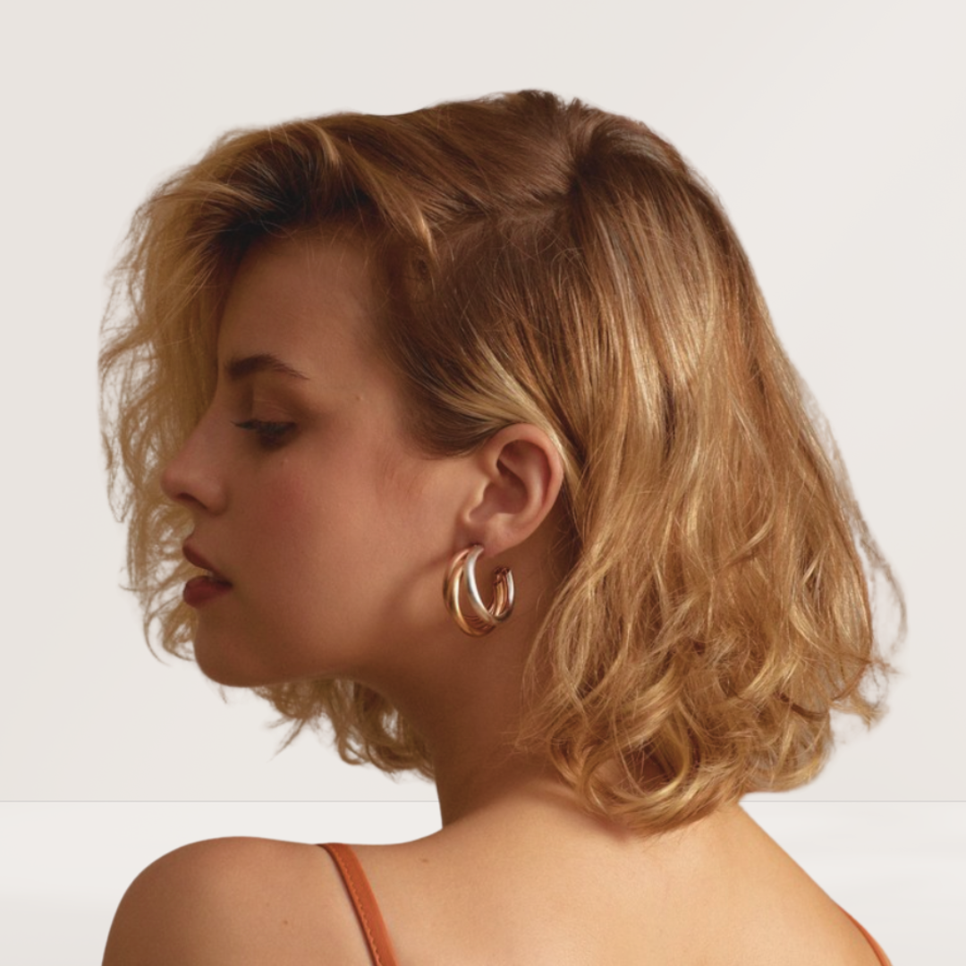 Woman with blonde hair wearing gold hoop earrings on a plain background