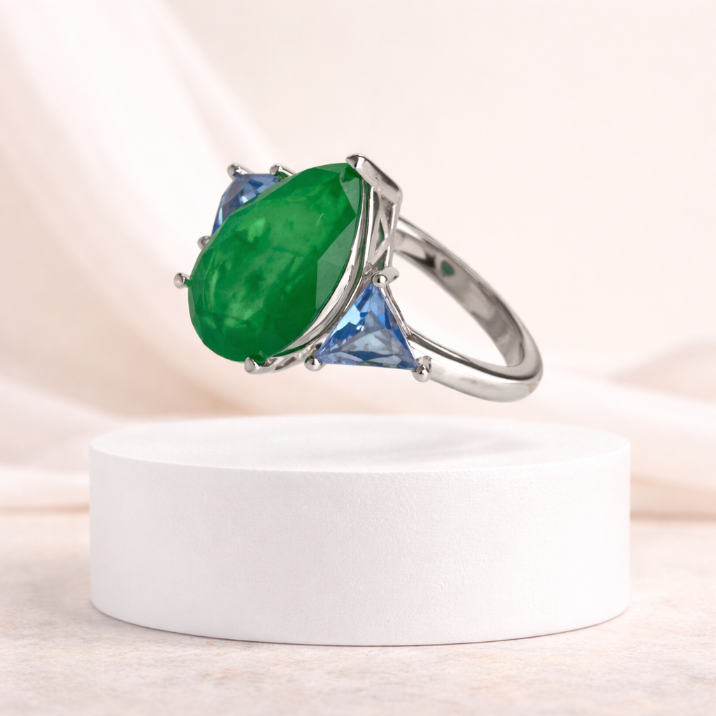 Silver ring with green gemstone on a white pedestal against a soft beige background