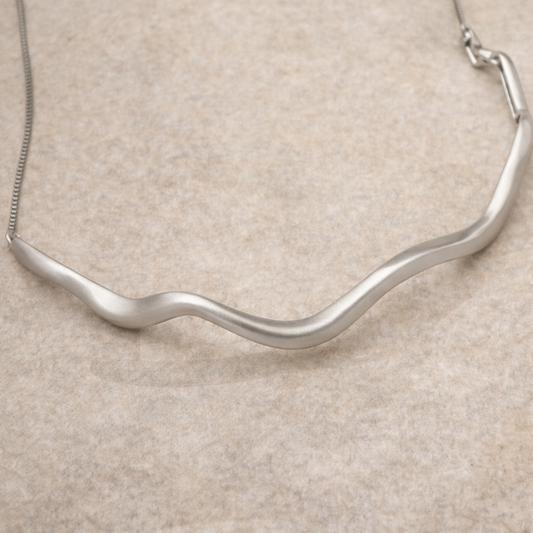 Silver necklace with a wavy design on a beige background