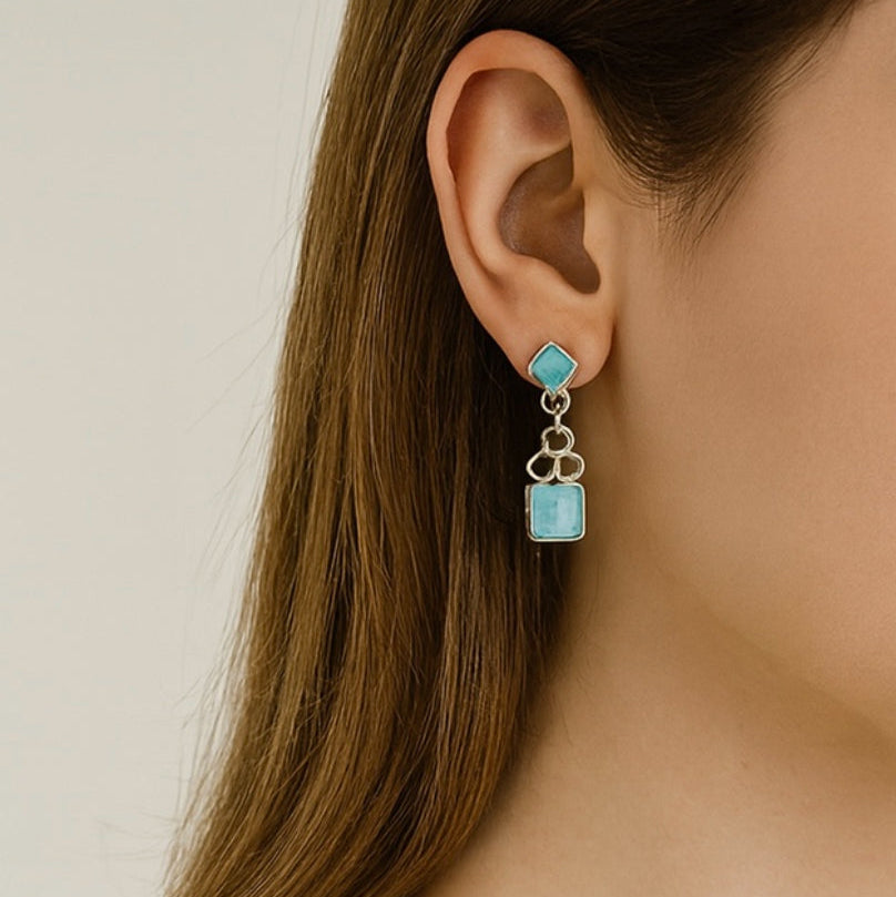 Close-up of an ear wearing a turquoise earring with a neutral background